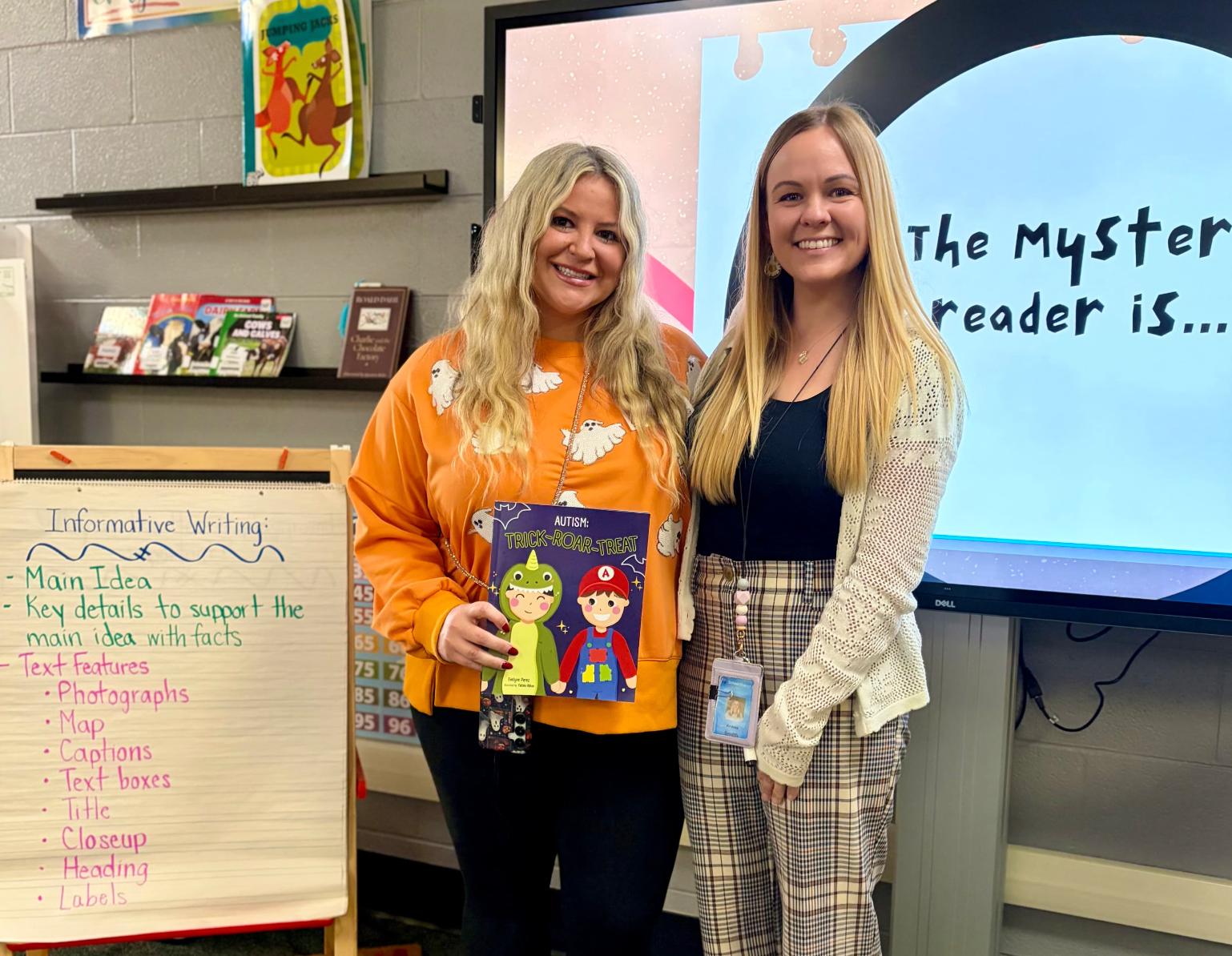 BCBA holds book and stands posed with teacher in a classroom